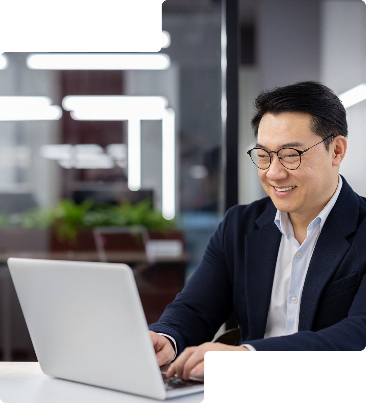 A person in a suit is smiling while typing on a laptop in a modern office setting.